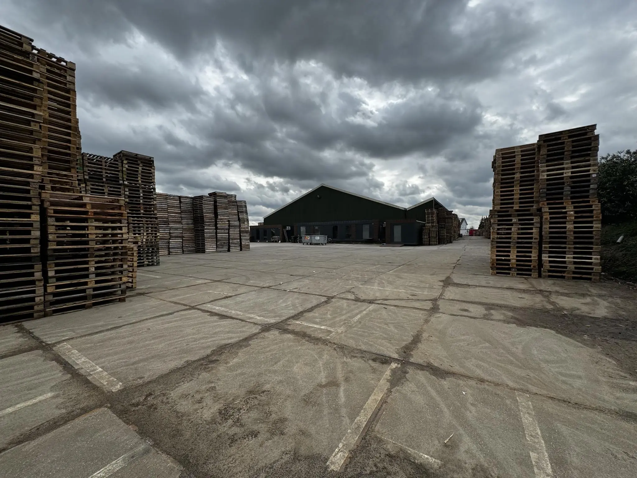 Stapels houten pallets op een industrieterrein aan de Graaf van Lynden van Sandenburgweg onder een dreigende, bewolkte lucht.